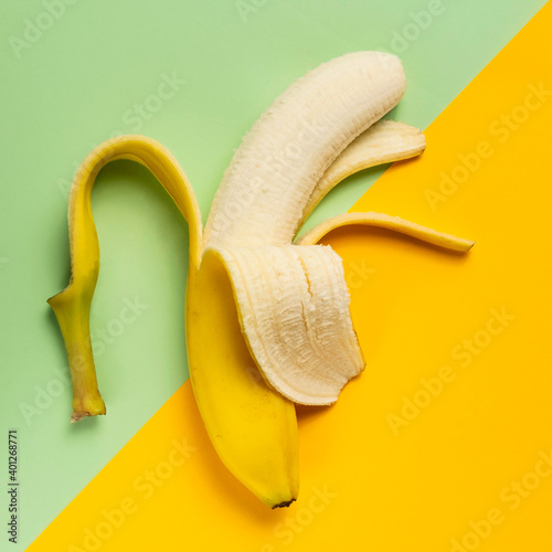 Half peeled banana on green and yellow background