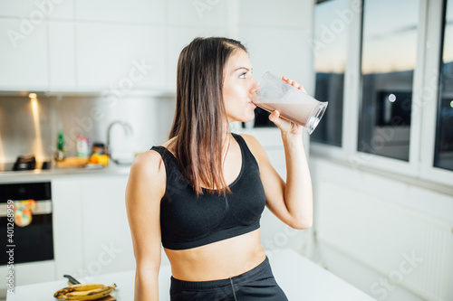 Woman in sportswear drinking sweet banana chocolate protein powder milkshake smoothie.Drinking protein after at home workout.Whey, banana and low fat milk sports nutrition diet.Healthy lifestyle