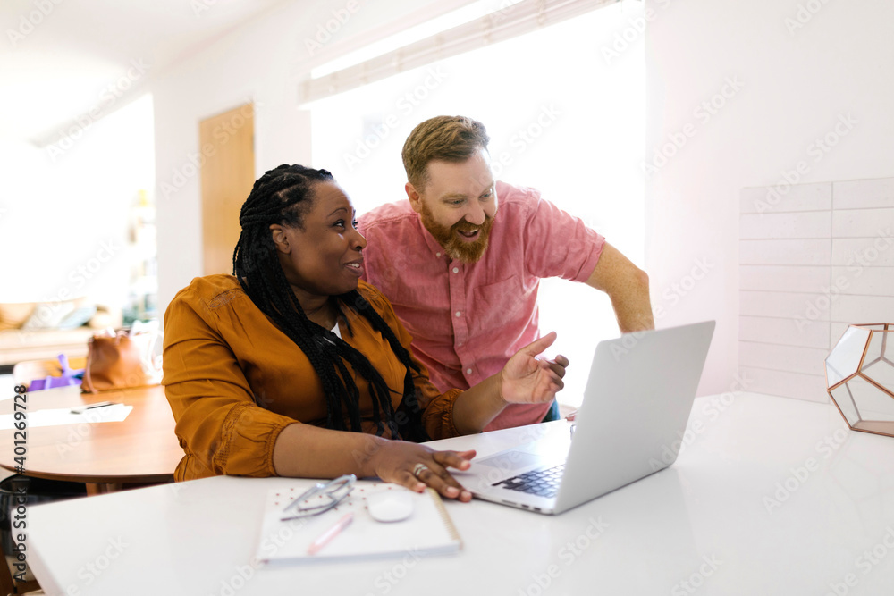 Smiling man and woman looking at laptop at desk in home office Smiling man and woman looking at laptop at desk in home office