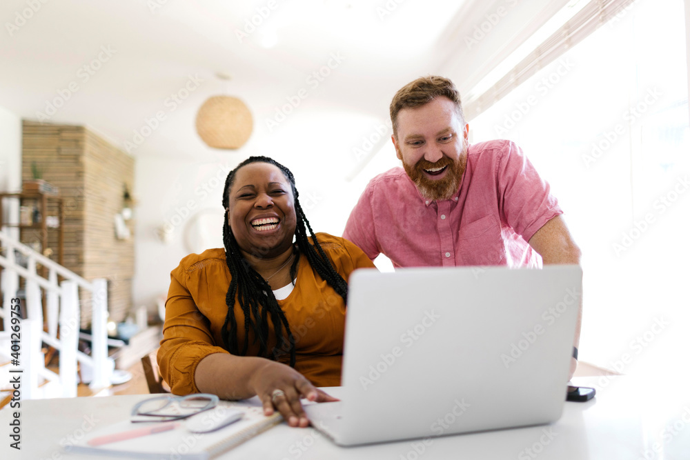 Man and woman looking at laptop at desk in home office Man and woman looking at laptop at desk in home office