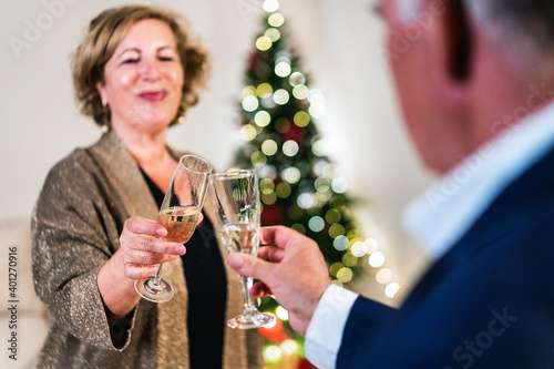 Delighted mature female clinking glass with champagne with crop friend while celebrating Christmas together photo