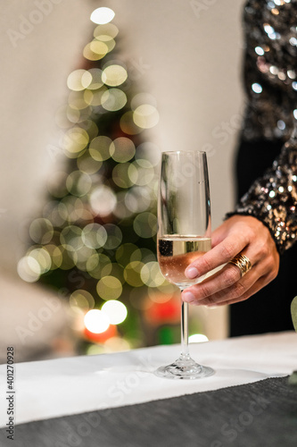 Unrecognizable female in glittering dress standing in room with glass of champagne during Christmas party