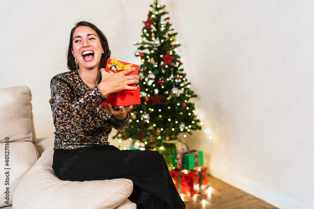Side view of excited female in elegant dress opening box and enjoying gift during Christmas celebration at home Side view of excited female in elegant dress opening box and enjoying gift during Christmas celebration at home