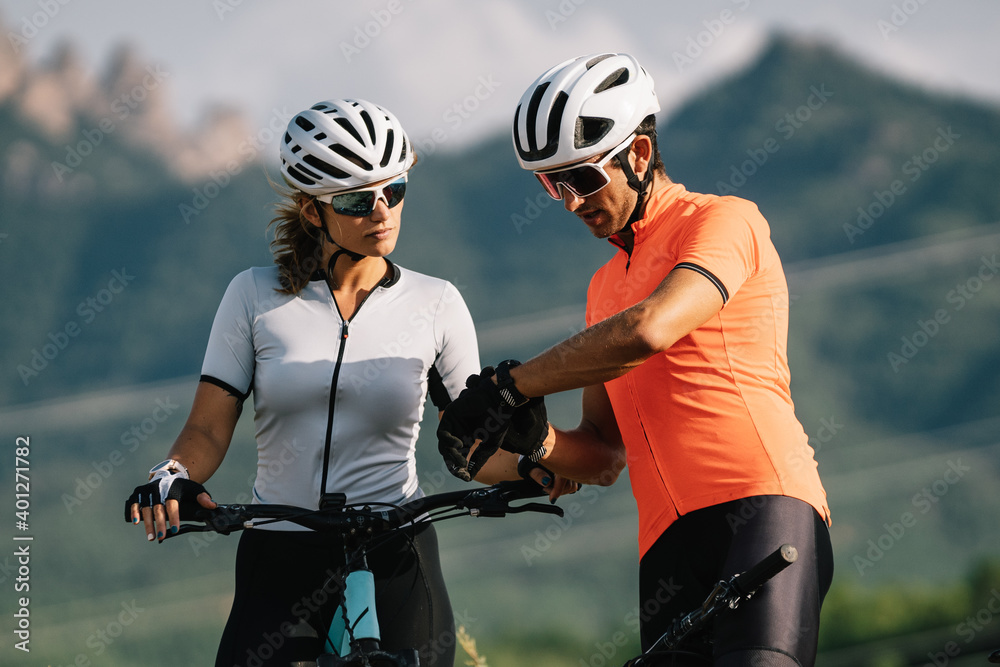 Bicyclists in helmets standing together on hill and checking time on wristwatch during training Bicyclists in helmets standing together on hill and checking time on wristwatch during training