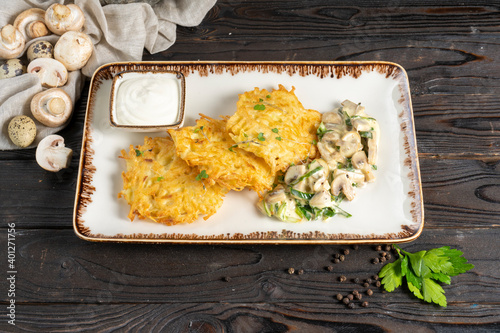 Draniki. Potato pancakes with mushrooms and sour cream. Traditional Belarusian hot second course of grated potatoes, mushrooms, herbs and sour cream in a ceramic plate on a wooden kitchen table. photo