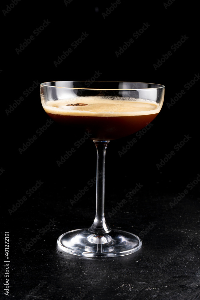 Espresso martini. Alcoholic cocktail of vanilla syrup, coffee liqueur, vodka and coffee beans in a transparent glass on a black background.