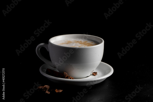 White coffee mug with spicy raf coffee and star anise on a saucer on a black background.