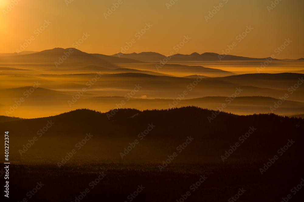 the sun sets below the horizon and illuminates the fog in the valley with a yellow light