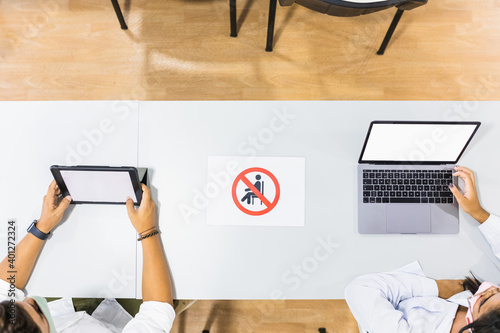 Top view of anonymous female coworkers using netbook and tablet with black screens while sitting at desk with prohibit sign photo