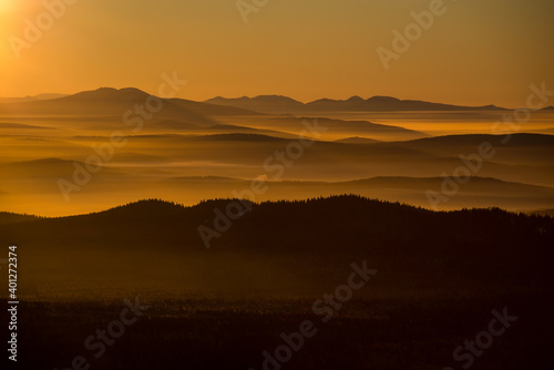 the sun sets below the horizon and illuminates the fog in the valley with a yellow light