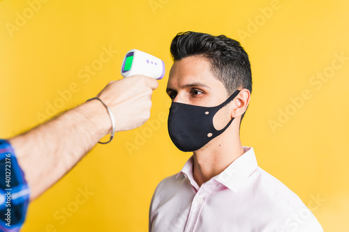 Crop unrecognizable male measuring temperature of happy colleague using digital thermometer on yellow background