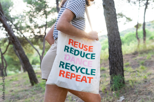 Side view of unrecognizable female walking in woods with reusable eco friendly bag while showing zero waste concept photo