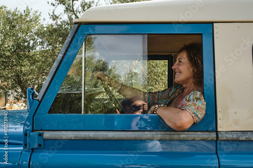 Wallpaper Mural Low angle side view of carefree mature female sitting on driver seat of old automobile parked in village and looking away Torontodigital.ca