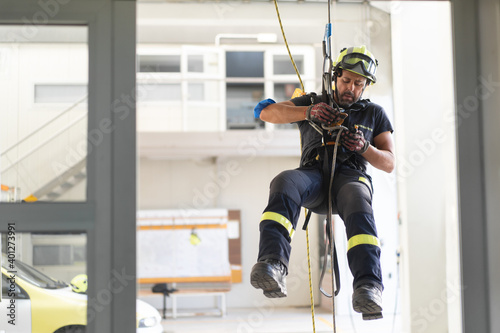 Young fireman in protective hardhat and gloves ascending wall on colorful rope during routine practices photo