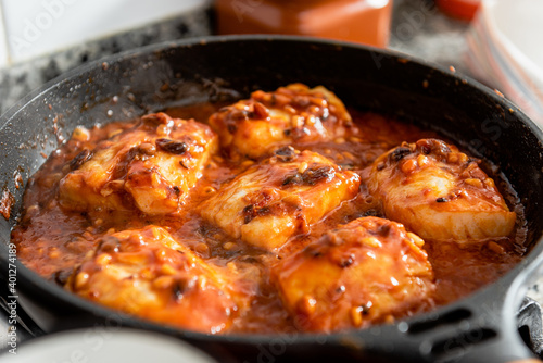 Closeup of frying pan with cod steaks and aromatic spicy red sauce with raisin and pine nuts placed on stove during preparation of typical Catalan dish