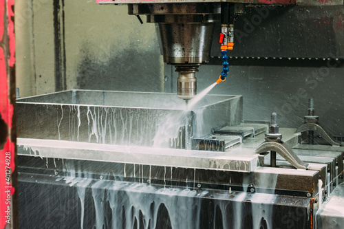 Foamy cutting fluids spraying on spinning metalworking equipment in light modern industrial workshop photo