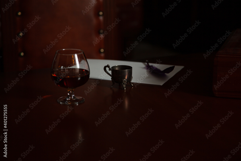 Glass of cognac and inkwell on polished table
