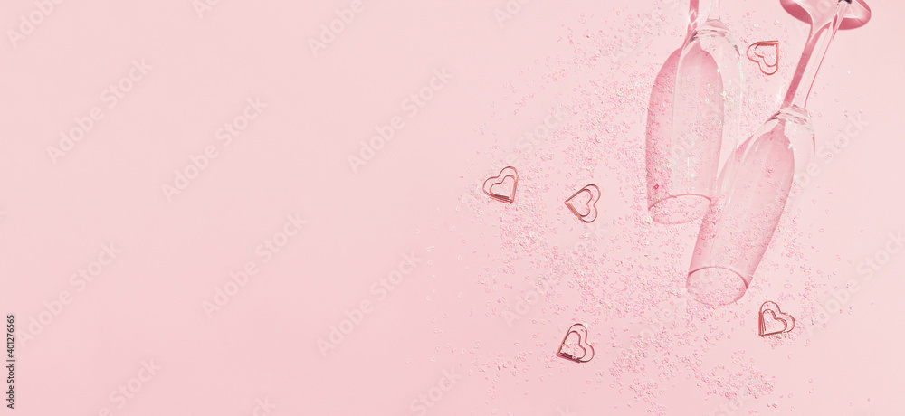 Two chrystal champagne glasses with heart shaped confetti on pastel pink background. Minimal style.