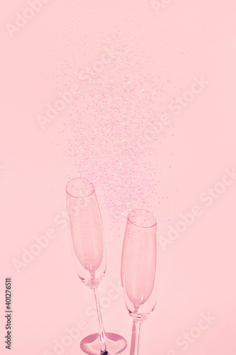Two chrystal champagne glasses with heart shaped confetti on pastel pink background. Minimal style.