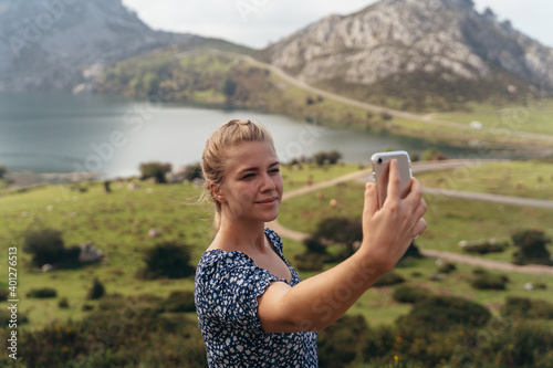 Side view of female with modern mobile phone taking selfie with amazing lush highland valley of background