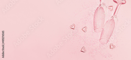 Two chrystal champagne glasses with heart shaped confetti on pastel pink background. Minimal style.