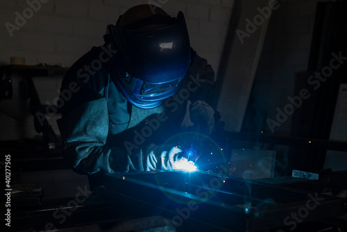Unrecognizable male employee in protective gloves and helmet using welding machine while working in dark workshop