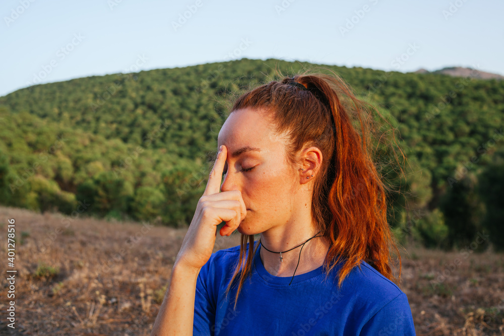Side view of relaxed flexible female sitting in Lotus pose and meditating with closed eyes on mat on meadow at sundown Side view of relaxed flexible female sitting in Lotus pose and meditating with closed eyes on mat on meadow at sundown