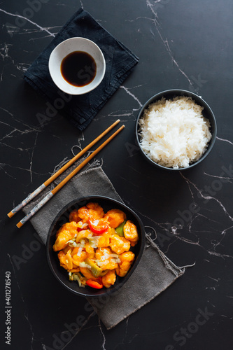 Top view of bowls with delicious rice and sweet and sour chicken dish placed on table with Asian chopsticks and soy sauce photo