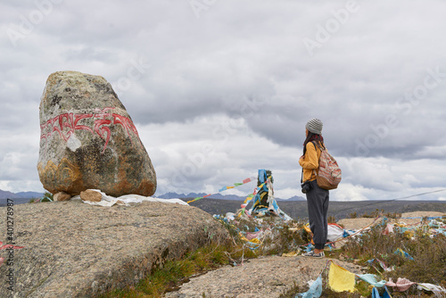 Full body side view of female tourist in warm clothing and hat looking at large stone with Om Mani Padme Hum mantra on surface in village of Baiyu in China photo