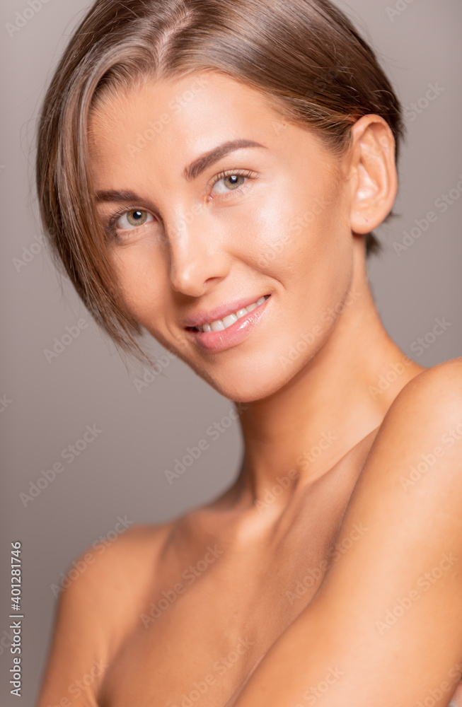 Charming female model with short hair and bare shoulders standing on violet background in studio and smiling at camera Charming female model with short hair and bare shoulders standing on violet background in studio and smiling at camera