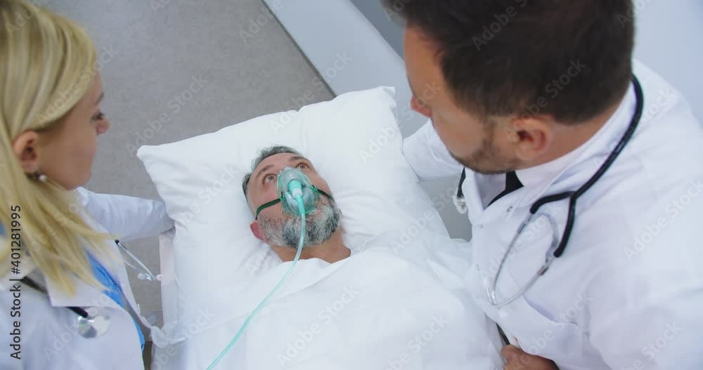 Emergency Department. View from above of doctors moving male patient lying on stretcher through hospital corridors putting on patient oxygen mask. Coronavirus pandemic. Covid-19 concept. Close up