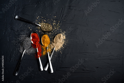 Spices in metal spoon on black background