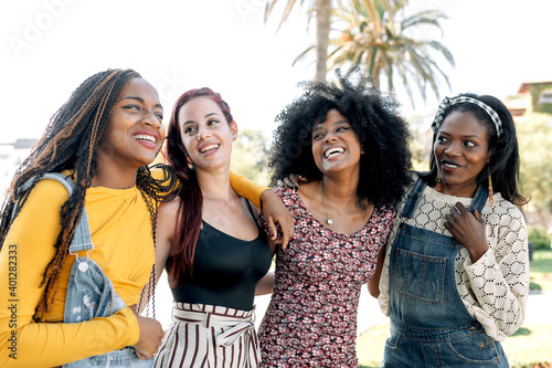 Friendly multiracial group of female friends cuddling on street while spending weekend in summer together