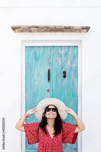 Female traveler in trendy apparel with arms holding hat and sunglasses near aged building in Greece photo