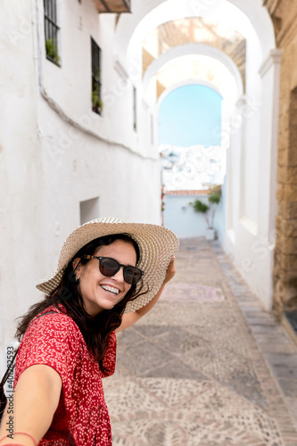 Side view of cheerful female traveler in straw hat on walkway between old buildings in White Village in Rhodes photo