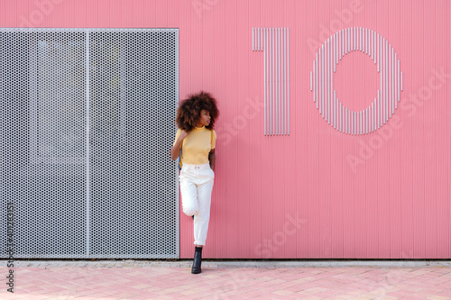 Black woman with afro hair posing in front of a pink wall looking away photo
