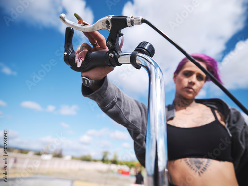 From below determined tattooed female in stylish outfit sitting on BMX bicycle in skate park and looking at camera photo