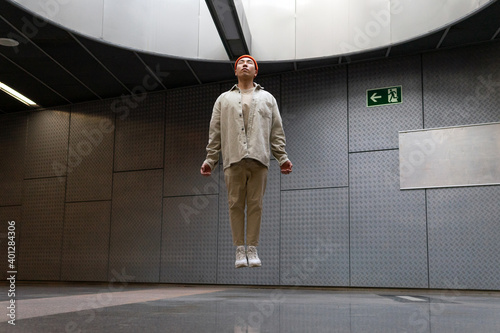 Full body focused stylist Asian male wearing casual outfit levitating with eyes closed above floor in building hallway