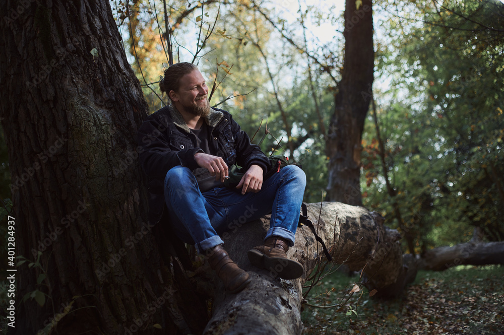 Portrait of a smoking young bearded man adventurer relaxing in the autumn forest and holding a cigarette