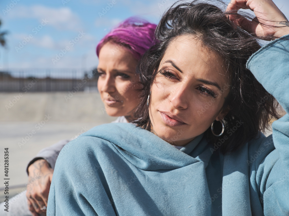 Women with tattoos sitting on ground in skate park and looking away while relaxing at weekend Women with tattoos sitting on ground in skate park and looking away while relaxing at weekend