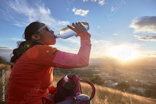 Side view of thirsty female drinking fresh water while resting on hill at sunny sundown
