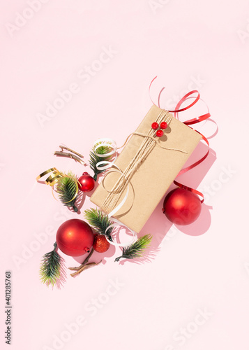 Top view of gift wrapped in craft paper and tied with twine arranged on pink background with Christmas baubles and various decorations