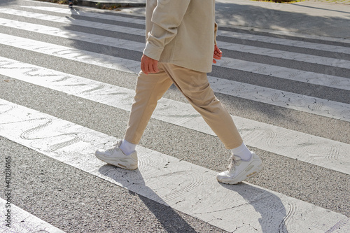 Cropped unrecognizable male pedestrian wearing casual outfit crossing on zebra crosswalk on the street on sunny day