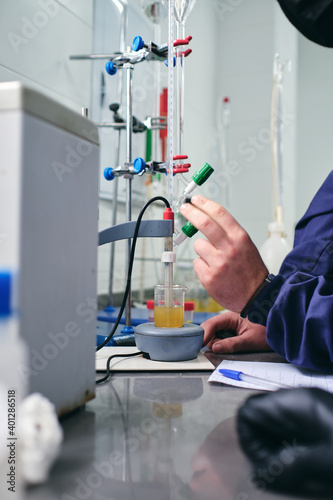 Hand of unrecognizable male chemist pouring liquid into flask while performing chemical experiment in laboratory