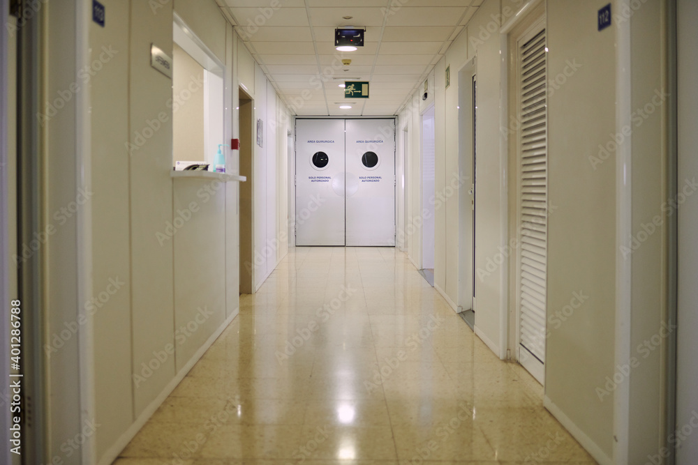 Doors in empty passage with glowing tiled floor illuminated by lamps in modern clinic Doors in empty passage with glowing tiled floor illuminated by lamps in modern clinic