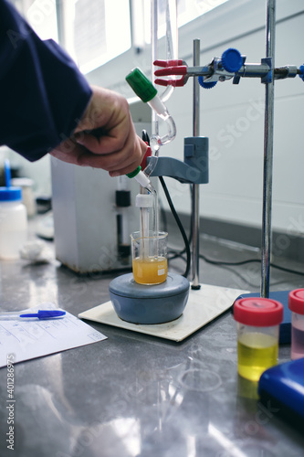 Hand of unrecognizable male chemist pouring liquid into flask while performing chemical experiment in laboratory
