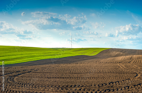 plowed field and winter wheat in the hilly terrain with cloudly sky of Ukraine