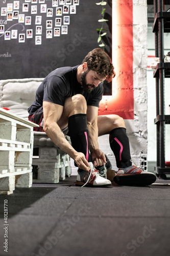 Focused athletic male weightlifter putting on sport shoes before workout in modern gym