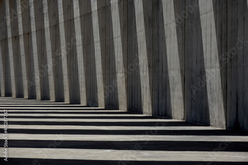 Columns of empty concrete walkway illuminated by sunlight casting lines of shadow on stone wall