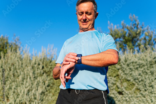 Senior athlete in sportswear standing outdoors in the street and checking the time on his smart watch after running